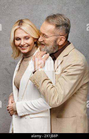 Ein eleganter, reifer Mann und eine Frau stehen in stilvollen Outfits vor grauem Hintergrund zusammen. Stockfoto