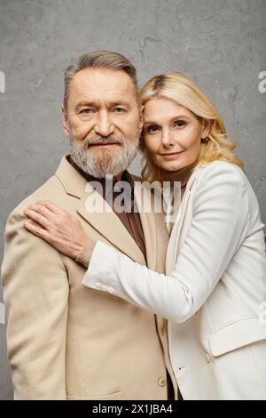 Ein reifes Paar, das elegant gekleidet ist, posiert zusammen vor einem grauen Hintergrund. Stockfoto