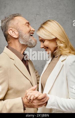 Elegantes, reifes, liebevolles Paar in Debonair-Kleidung steht zusammen vor grauem Hintergrund. Stockfoto