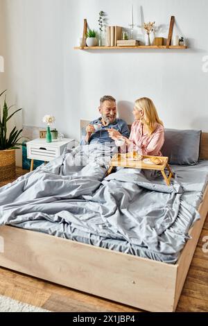 Ein reifes, liebevolles Paar in gemütlicher Hauswäsche sitzt eng zusammen auf einem Bett in ihrem Schlafzimmer und teilt einen ruhigen Moment. Stockfoto