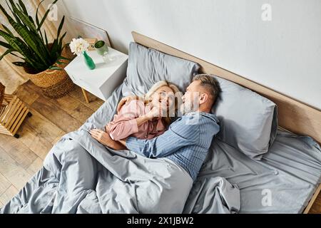 Ein reifes, liebevolles Paar in Homewear kuschelt und entspannt sich zusammen auf einem Bett, um einen ruhigen Moment der Intimität zu teilen. Stockfoto