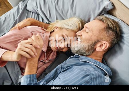 Ein reifes, liebevolles Paar in gemütlicher Hauswäsche lag friedlich auf einem Bett und teilte sich eine zarte Umarmung in ihrem Schlafzimmer. Stockfoto