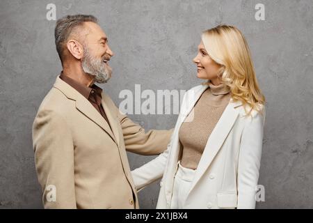 Ein eleganter, reifer Mann und eine Frau stehen in Debonair-Kleidung vor grauem Hintergrund nebeneinander. Stockfoto