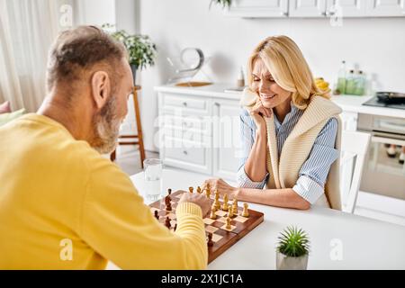 Ein reifes, liebevolles Paar in kuscheligen Haushaltswaren, das zu Hause ein strategisches Schachspiel spielt. Stockfoto