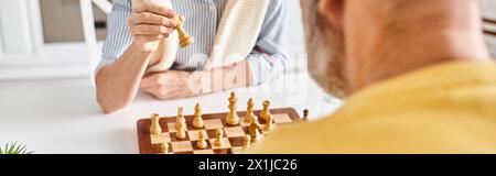 Ein Mann in kuscheliger Homewear spielt in einem strategischen Schachspiel mit einer riesigen Banane in einer skurrilen und surrealen Umgebung zu Hause. Stockfoto