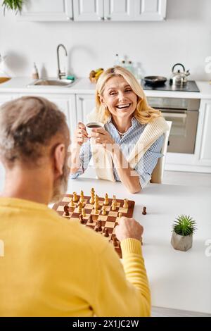 Ein reifes, liebevolles Paar in kuscheliger Homewear spielt in ihrer Küche ein anspruchsvolles Schachspiel, fokussiert und nachdenklich. Stockfoto