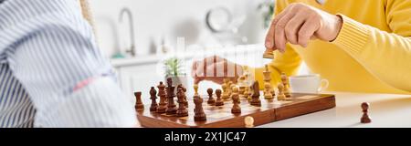 Ein reifes, liebevolles Paar in kuscheliger Homewear, das sich intensiv auf ein Schachspiel konzentriert und über die nächsten Moves nachdenkt. Stockfoto