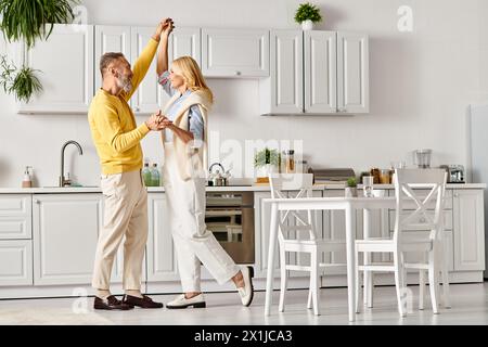 Ein reifes, liebevolles Paar in kuscheliger Homewear, das zu Hause fröhlich in der Küche tanzt. Stockfoto