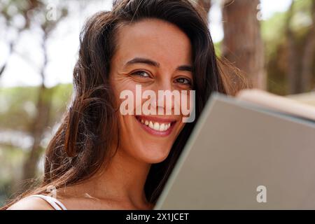 Eine junge Frau lächelt und blickt in die Kamera mit einem offenen Buch in der Hand Stockfoto