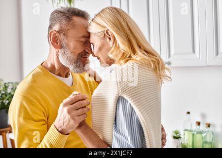 Ein reifes, liebevolles Paar in gemütlicher Homewear umarmt sich in ihrer Küche und teilt einen Moment der Zweisamkeit. Stockfoto