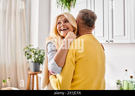Ein reifes, liebevolles Paar in kuscheliger Homewear, das sich in der Küche ihres Hauses warm umarmt. Stockfoto