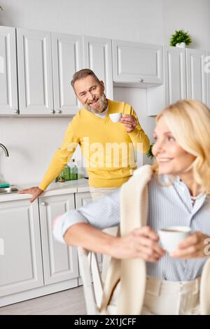 Ein reifes, liebevolles Paar in gemütlichen Haushaltswaren, das zusammen in einer Küche zu Hause steht und einen besonderen Moment teilt. Stockfoto