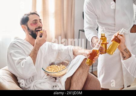 Ein Mann in einem Stuhl, der neben seinen verschiedenen Freunden eine Schüssel Popcorn und eine Flasche Bier genießt, mit einem Gefühl der Entspannung und Zufriedenheit. Stockfoto