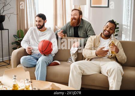 Drei fröhliche, interrassische Freunde sitzen zusammen auf einer Couch in lässiger Kleidung und genießen eine tolle Zeit zu Hause. Stockfoto
