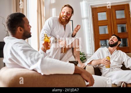 Drei fröhliche Männer mit unterschiedlichem Hintergrund lachen in einem gemütlichen Wohnzimmer, während sie Bademäntel tragen. Stockfoto