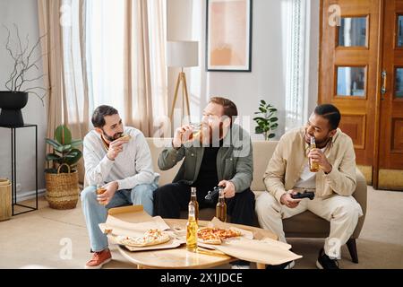 Drei fröhliche, interrassische Männer in lässiger Kleidung, die Pizza und Bier auf einer Couch genießen und Freundschaft und Kameradschaft ausdrücken. Stockfoto