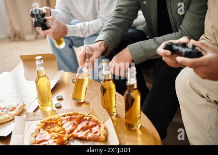 Drei gutaussehende Freunde verschiedener Rassen genießen Pizza und Bier an einem Tisch in gemütlicher Umgebung, die Freude und Kameradschaft ausstrahlen. Stockfoto