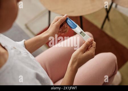 Hochwinkelnaht weiblicher Hände, die Schwangerschaftstest halten, mit leerem Bildschirm, der auf Sofa im Kopierraum sitzt Stockfoto