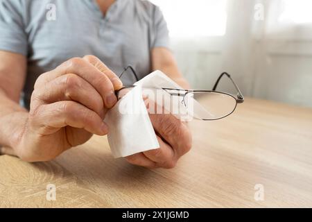 Reife männliche Hände reinigen Gläser mit dünnem Metallrahmen sorgfältig und betonen so die Gesundheit des Sehens, die Pflege von Brillen und die persönliche Hygiene, die visuelle Klarheit, Stockfoto