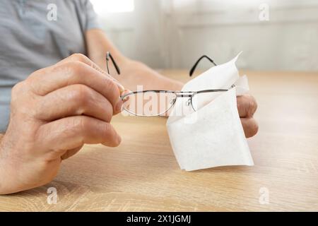 Reife männliche Hände reinigen Gläser mit dünnem Metallrahmen sorgfältig und betonen so die Gesundheit des Sehens, die Pflege von Brillen und die persönliche Hygiene, die visuelle Klarheit, Stockfoto