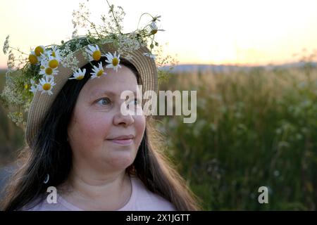 Glückliche lächelnde Frau im Blumenkranz auf grüner sonniger Wiese, Blumenkrone, Sommersonnenwende, traditionelle slawische Zeremonie am Mittsommer, wiccan Litha sabb Stockfoto