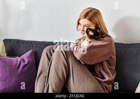 Eine Frau mit kurzen Haaren entspannt sich auf einer Couch und legt ihre Katze in die Arme, während sie einen ruhigen Moment miteinander verbringen. Stockfoto