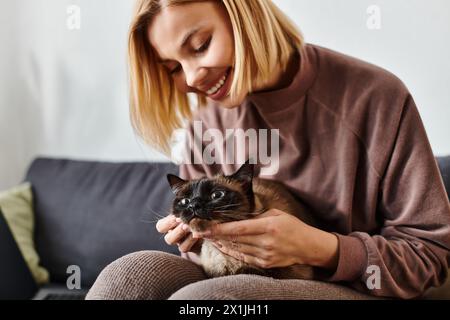 Eine Frau mit kurzen Haaren sitzt friedlich auf einer Couch und streichelt ihre Katze. Stockfoto