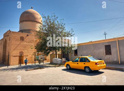 Samarkand, USBEKISTAN - 18. SEPTEMBER 2023: Gelbes Taxi und Moschee in der Nähe des Gur-Emir-Mausoleums vor blauem Himmel Stockfoto