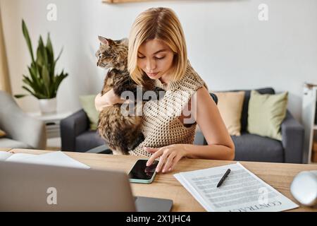 Eine Frau mit kurzen Haaren sitzt an einem Tisch und streichelt ihre Katze auf ihrem Schoß, was eine ruhige Atmosphäre schafft. Stockfoto