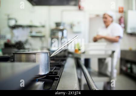 Kochtopf in der Industrieküche der Schule mit dem Koch im Hintergrund vor der Mittagszeit aufwärmen Stockfoto