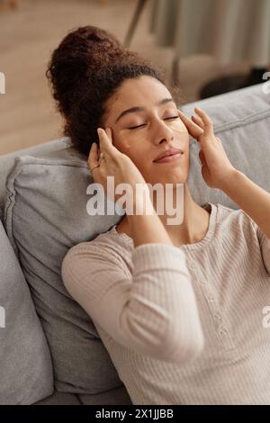 Vertikales Hochwinkelporträt einer jungen Frau, die sich zu Hause selbst kümmert und Gesichtsmassagen macht Stockfoto