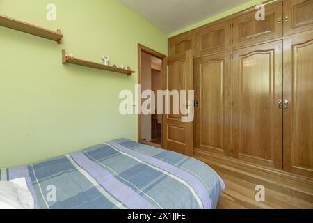 Classic-Schlafzimmer mit einem Bett mit gestreiftem Bettüberwurf, einem großen Einbauschrank mit Eichenholztüren und hellgrün gestrichenen Wänden Stockfoto