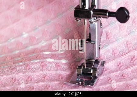 Eine Nadel mit Nadelhalter und Nähmaschinenfuß auf einem Hintergrund aus rosa Stoff. Makro, Industrie. Kopierbereich für Text Stockfoto