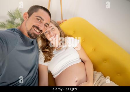 Eine schwangere Frau und ihr Mann fotografieren sich zu Hause auf dem Handy. Stockfoto