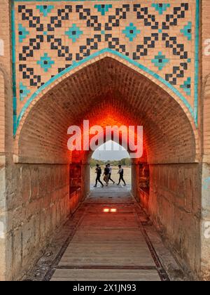 Ein Blick durch den beleuchteten gewölbten Bogen der Khaju-Brücke aus dem 17. Jahrhundert auf dem Fluss Zayanderud während der Trockenzeit mit trockenem Flussbett. Isfahan, Iran. Stockfoto