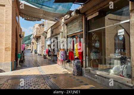 Eine enge Kopfsteinpflasterstraße mit Sonnenschutzdach, gesäumt von kleinen Geschäften im historischen Zentrum von Isfahan, Iran. Stockfoto