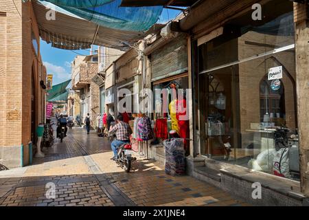 Eine enge Kopfsteinpflasterstraße mit Sonnenschutzdach, gesäumt von kleinen Geschäften im historischen Zentrum von Isfahan, Iran. Stockfoto