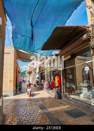 Eine enge Kopfsteinpflasterstraße mit Sonnenschutzdach, gesäumt von kleinen Geschäften im historischen Zentrum von Isfahan, Iran. Stockfoto