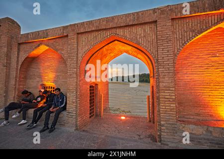 Junge iranische Männer sitzen auf der Allahverdi Khan-Brücke, auch bekannt als Si-o-se-pol (17. Jahrhundert), beleuchtet in der Abenddämmerung. Isfahan, Iran. Stockfoto