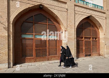 Zwei junge iranische Frauen in schwarzen Chadors gehen gemeinsam auf dem Naqsh-e Jahan-Platz, dem UNESCO-Weltkulturerbe. Isfahan, Iran. Stockfoto