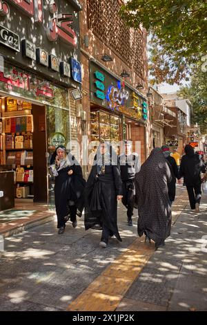 Iranische Frauen in traditionellen schwarzen Chadors gehen entlang einer engen Straße im historischen Zentrum von Isfahan, Iran. Stockfoto