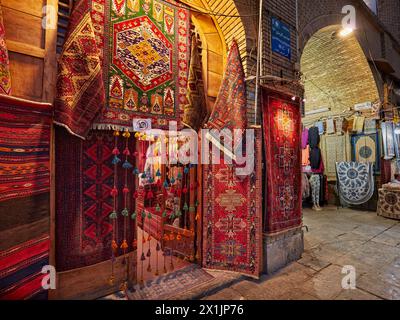 Eine Auswahl an handgefertigten persischen Teppichen, die am Eingang eines Kunsthandwerksgeschäfts auf dem bei Nacht beleuchteten Platz Naqsh-e Jahan ausgestellt werden. Isfahan, Iran. Stockfoto