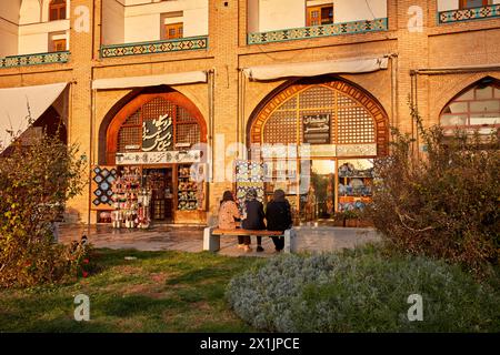 Drei iranische Frauen sitzen auf einer Bank vor einem Schaufenster eines Kunsthandwerks auf dem Naqsh-e Jahan-Platz, dem UNESCO-Weltkulturerbe. Isfahan, Iran. Stockfoto