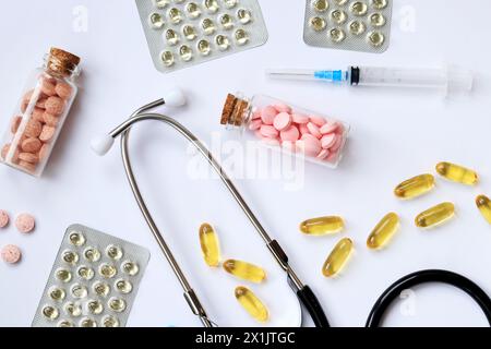 Stethoskop auf weißem Hintergrund, Draufsicht. Medizinisches Instrument und verschiedene Medikamente, Tabletten, Kapseln und Spritzen. Medizin und Gesundheitswesen Stockfoto
