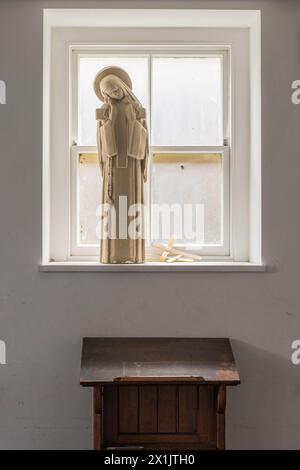 Ein Prie-dieu oder Gebetstisch in einem ruhigen Raum unter einem Fenster, mit einer Marienstatue und zwei Palmenkreuzen Stockfoto