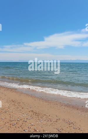 Strand mit Wellen und nassem Sand mit Kieselsteinen auf blauem Himmel und Bergen. Meer, Ozean Hintergrund. Urlaub Outdoor und Reise Urlaub Abenteuer Konzept. Vert Stockfoto