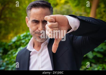 Seriöser Geschäftsmann mit Daumen nach unten und Blick auf die Kamera im Freien. Stockfoto