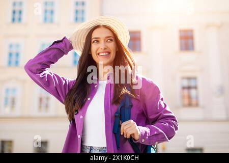 Lächelnde junge Frau, die draußen Strohhut berührt Stockfoto
