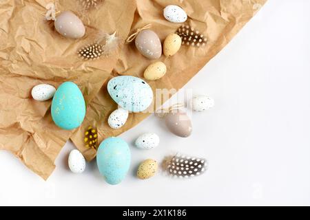 Ostereier und Federn auf braunem Kraftpapierhintergrund auf einem weißen Tisch. Draufsicht. Für ostergrußkarten mit Kopierraum. Stockfoto