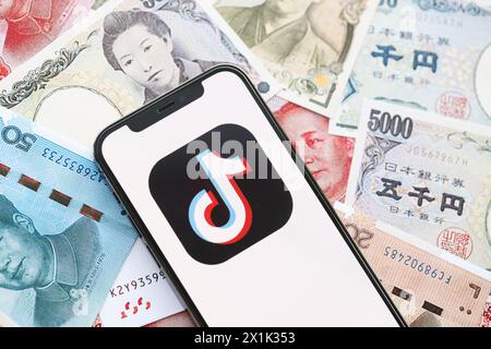 KIEW, UKRAINE - 1. APRIL 2024 TikTok oder Douyin Symbol auf dem Smartphone-Bildschirm auf vielen asiatischen Geldrechnungen. IPhone-Display mit App-Logo mit japanischen Yen- und chinesischen Yuan-Banknoten Stockfoto